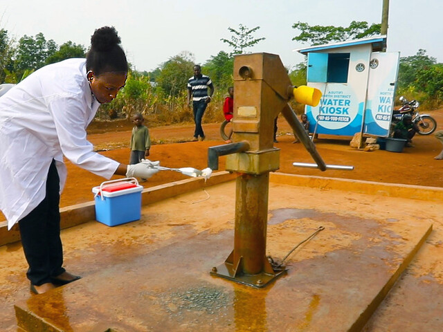 Janet Atebiya purifying the mouth of the pump at Kenyasi, before testing the water for E. coli