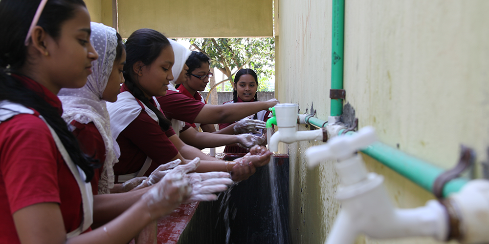 Teenaged girls washing hands at communal school sink